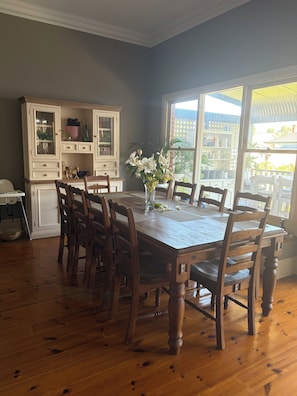 A dining room with a wooden table and chairs, a cabinet with glass doors, and a window with a view of buildings. - Somewhere Special, Pool, Steam Sauna, Outdoor Bar, Fireplace (Woodville Park)