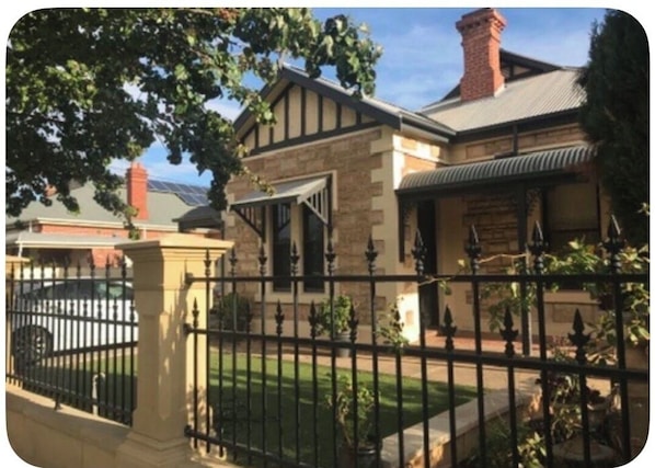 A two-story house with a stone facade, a visible chimney, and a black metal fence. - Somewhere Special, Pool, Steam Sauna, Outdoor Bar, Fireplace (Woodville Park)