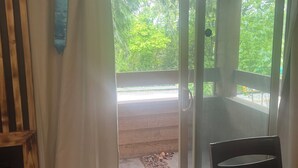 Una stanza con una porta a vetri scorrevoli che dà su uno spazio esterno con terrazza in legno e vegetazione.