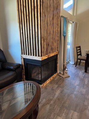 A living room with a fireplace, a glass coffee table, a sofa, and a dining area with a chair. -  1-bedroom condo with gas heat (Seattle)