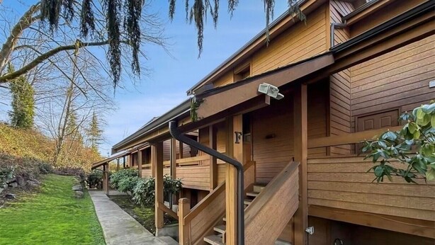 Un edificio in legno con un portico coperto, un vialetto in cemento e un piccolo giardino.