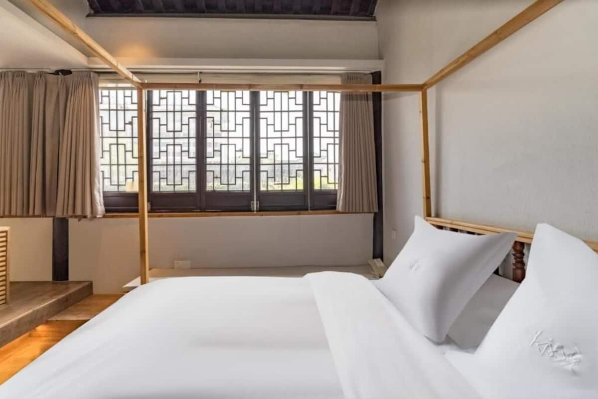 A room with a bed, window with curtains, wooden headboard, and a view of the outside.