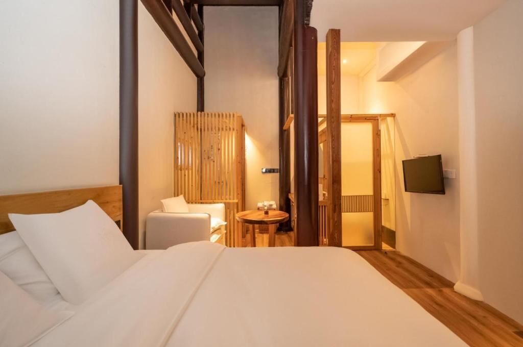 Camera d'albergo con un letto, un tavolino rotondo, una sedia, un televisore fissato al muro e un divisorio in legno.