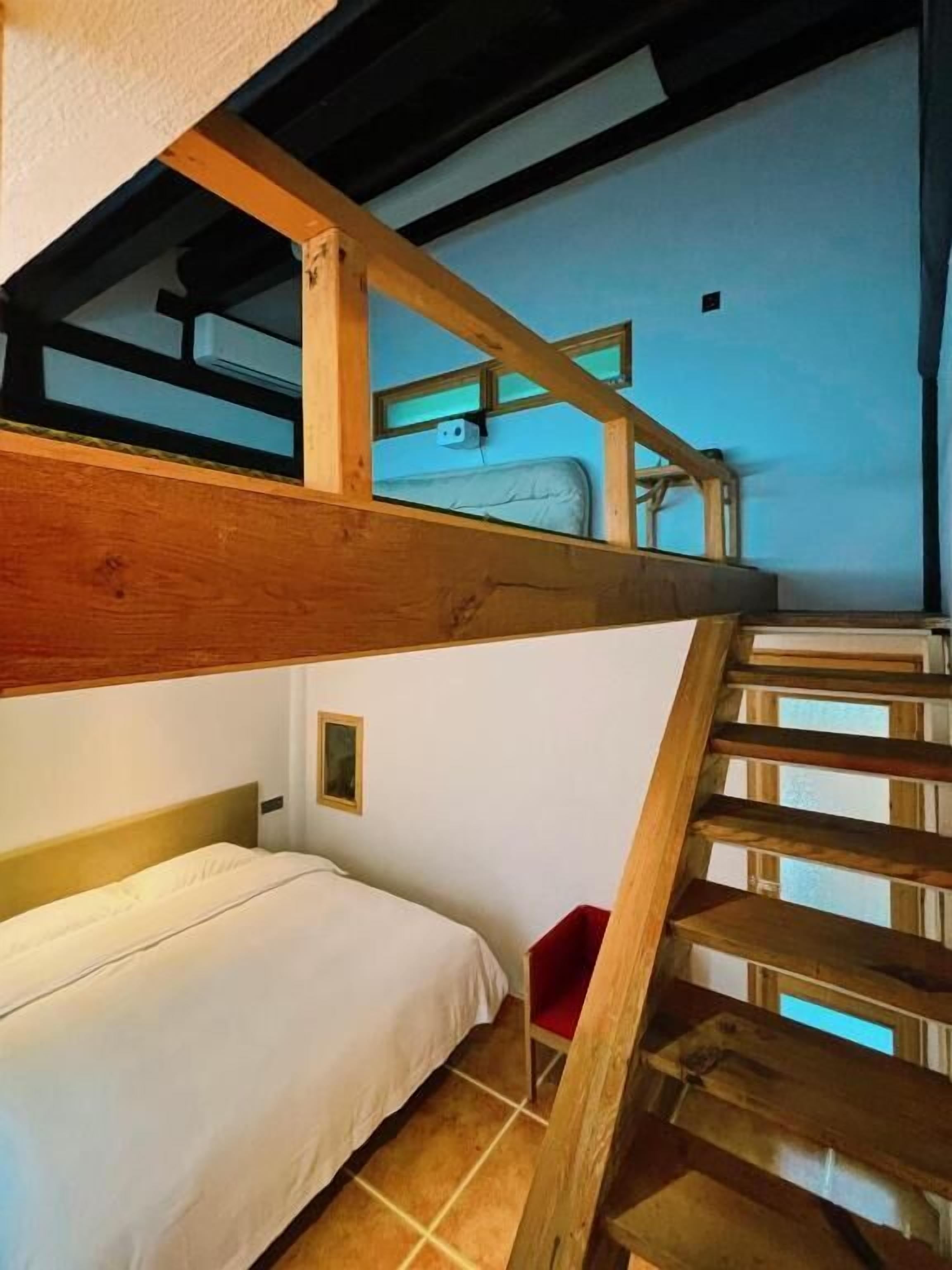 A bunk bed room with a wooden staircase and a small red chair.