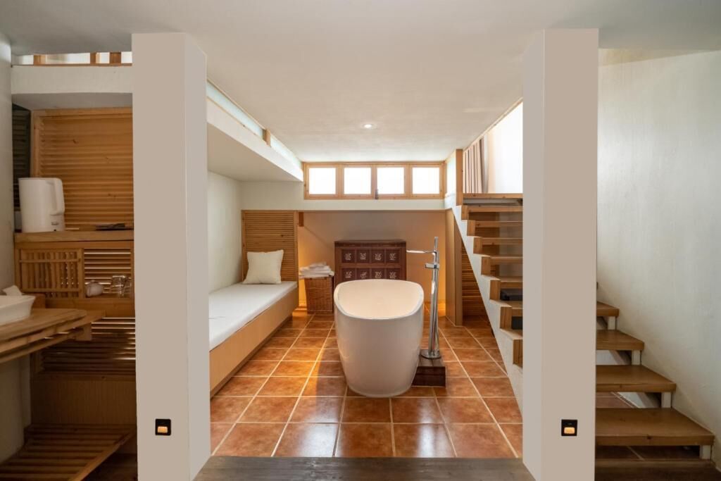 A modern bathroom with a bathtub, wooden flooring, and a staircase.