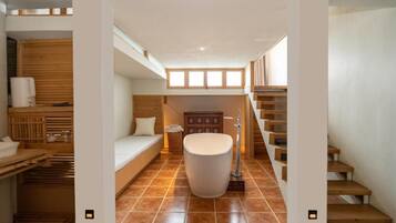A modern bathroom with a bathtub, wooden flooring, and a staircase.