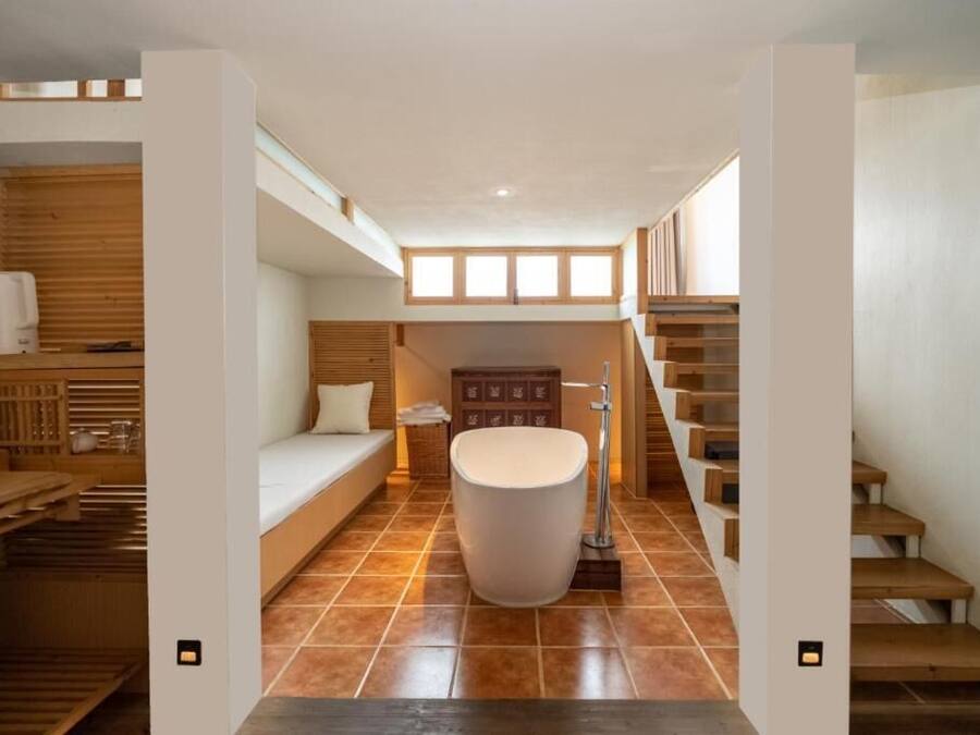 A modern bathroom with a bathtub, wooden flooring, and a staircase.