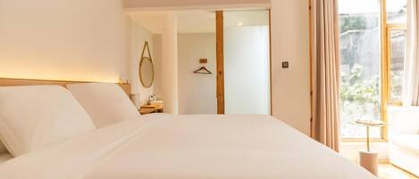 Un dormitorio con una cama grande, una mesita de noche, una lámpara colgante y vistas al exterior a través de una ventana.