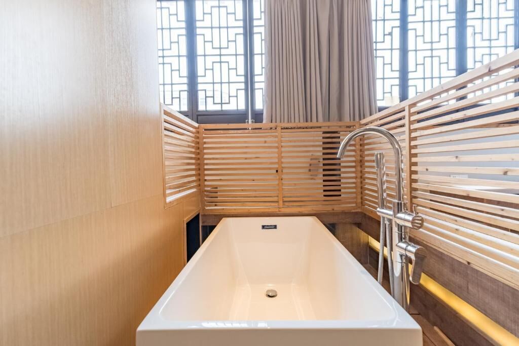 A modern bathroom with a rectangular bathtub, wooden slatted walls, and a window with a geometric pattern.