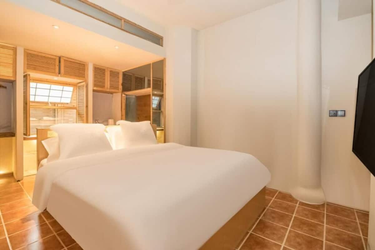 A hotel room with a large bed, wooden headboard, a TV, and a window with shutters.