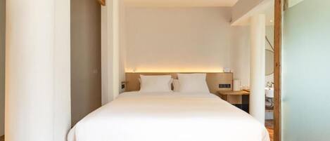 A modern hotel room with a large bed, a bedside table, and a nightstand.