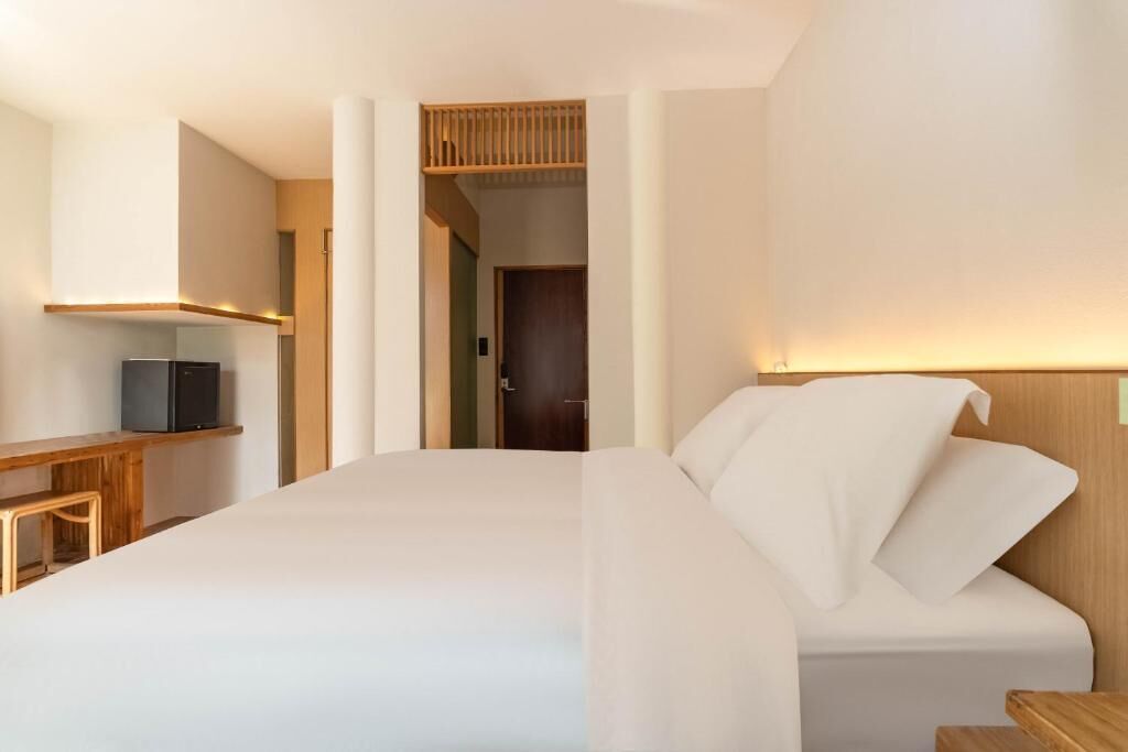 A modern hotel room with a large bed, a desk with a television, and a wooden headboard.