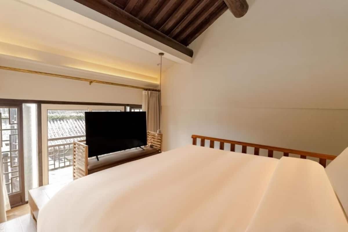 A bedroom with a bed, a television, and a balcony with a view.