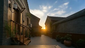A narrow outdoor corridor with wooden railings, potted plants, and a view of the sunset. - Cloud and Wind (Yangzhou)