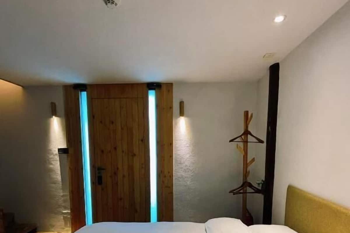 A bedroom with a bed, wooden door, wall-mounted lights, and a coat rack.