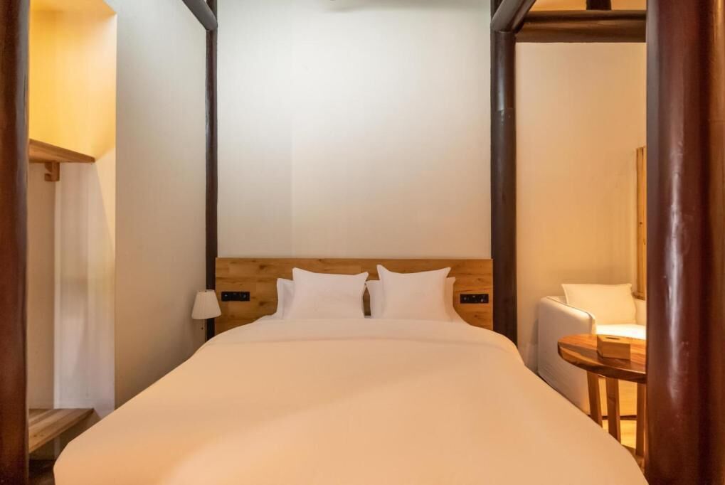 Habitación de hotel con una cama grande, cabecero de madera, mesitas de noche y una pequeña mesa redonda.