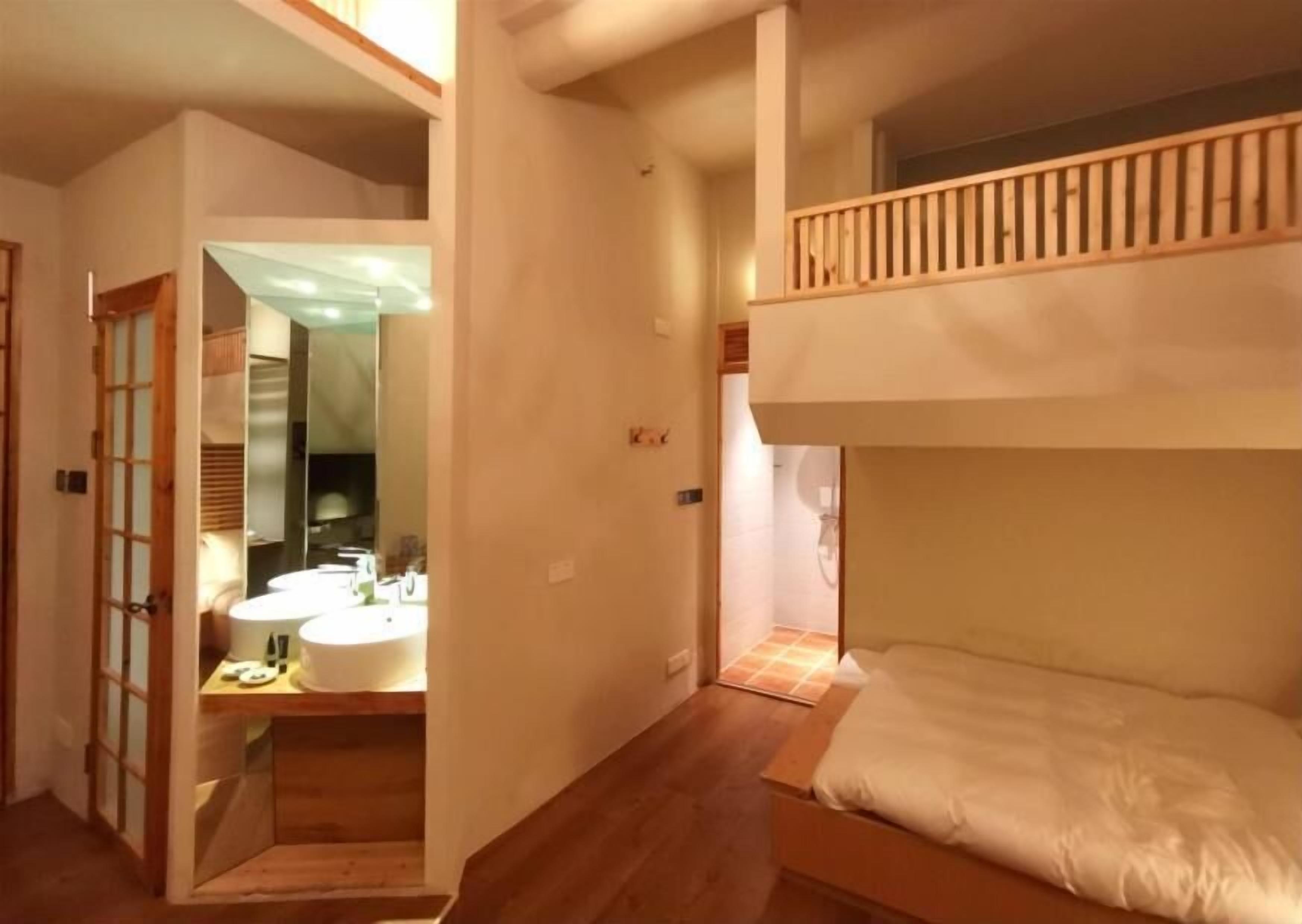 A room with a bunk bed, a wooden floor, a bathroom with a sink and mirror, and a door with a traditional design.
