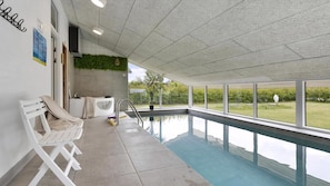 Ein moderner, überdachter Pool mit Glaswänden, einem Whirlpool und Blick ins Freie.