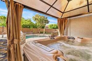 Ein Whirlpool mit Bedienfeld, umgeben von einer überdachten Terrasse, im Hintergrund ein Pool.