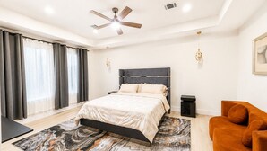 Une chambre moderne comprenant un lit, un ventilateur de plafond, une table de chevet, un canapé et un tapis à motifs de marbre.