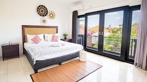 A modern bedroom with a large bed, a nightstand, a decorative wall piece, and a view of the outside. - Sunbeji Villa (Seminyak)