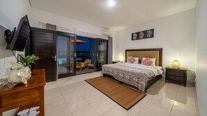 A bedroom with a bed, bedside tables, a TV, a sliding glass door, and a view of the outside. - Sunbeji Villa (Seminyak)