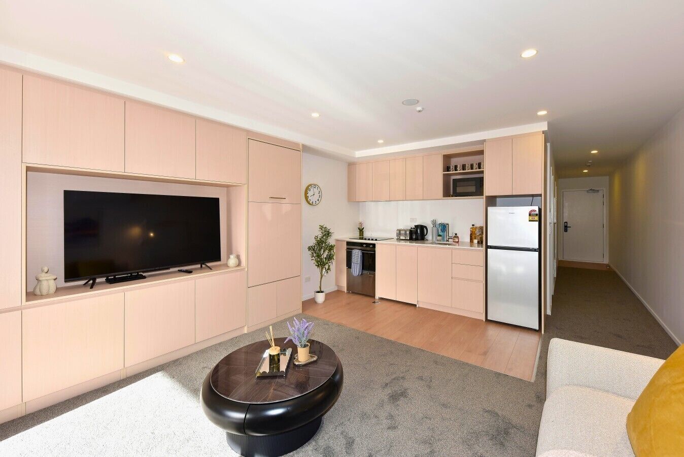 A modern apartment with a flat-screen TV, a dining area, a kitchen with a refrigerator, and a living room with a coffee table.