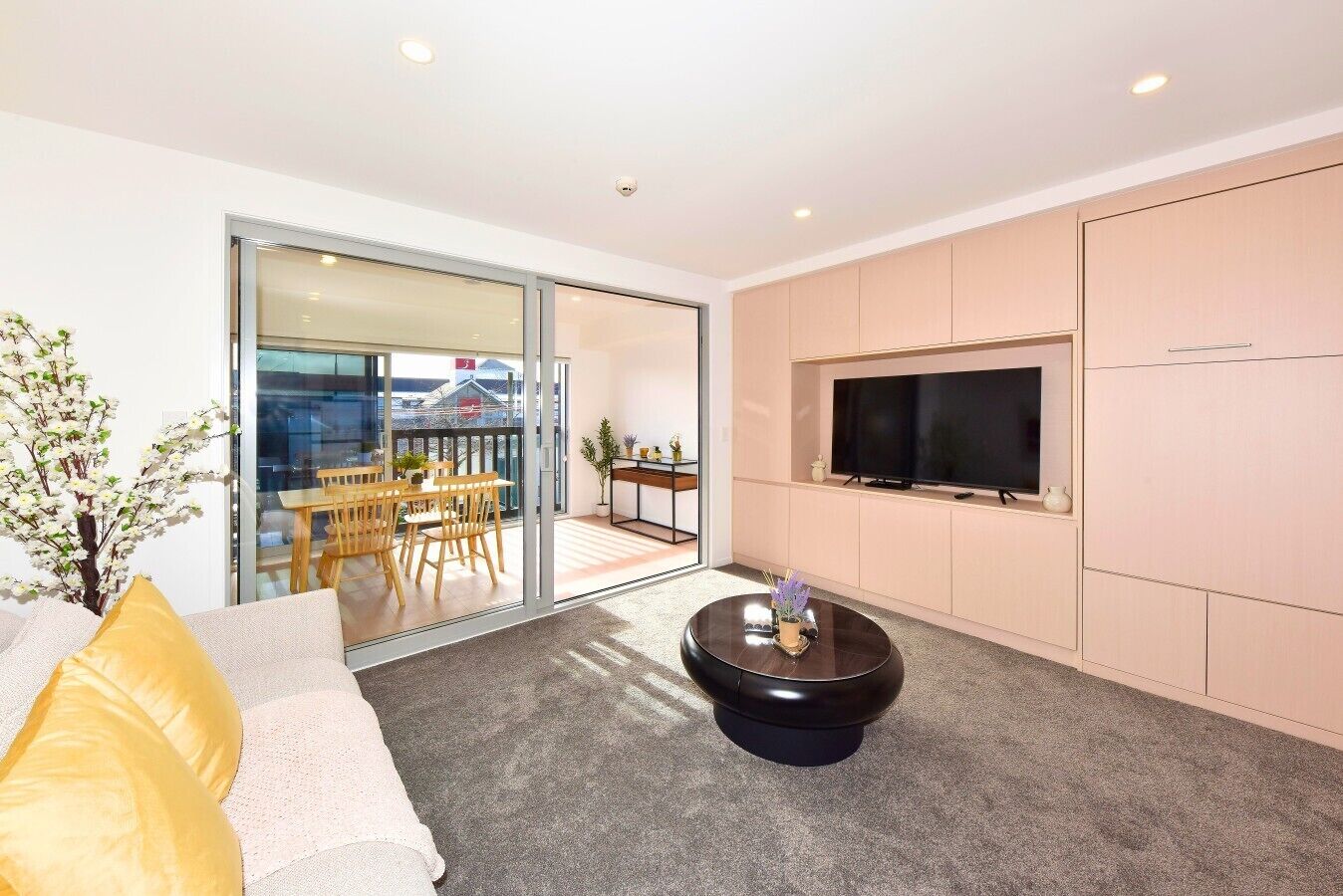 A modern living room with a sofa, a coffee table, a TV, and a sliding glass door leading to a balcony.