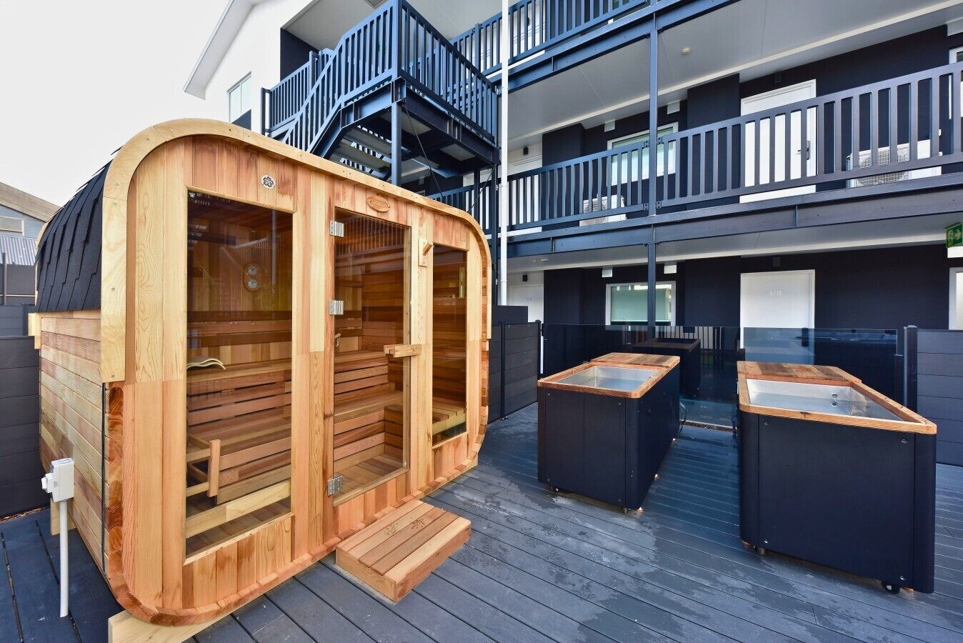 Una sauna con panche in legno e un'ampia vetrata, situata su una terrazza che include un tavolo da biliardo e un angolo cottura esterno.