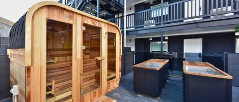 Una sauna con panche in legno e un'ampia vetrata, situata su una terrazza che include un tavolo da biliardo e un angolo cottura esterno.