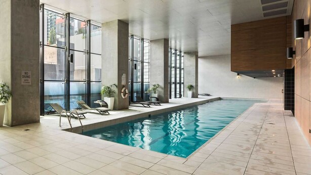 Une piscine intérieure avec des parois en verre transparent, des chaises longues et des plantes en pot.