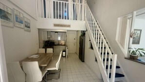 A dining area with a wooden table and chairs, a kitchen with white cabinets, and a staircase with white railings. - CHARMING HOUSE WITH PRIVATE SWIMMING POOL FOR 6 PEOPLE (STE MAXIME)