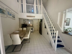 Ein Essbereich mit Holztisch und -stühlen, eine Küche mit weißen Schränken und eine Treppe mit weißen Geländern.