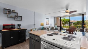 Een moderne keuken met een fornuis, magnetron en kasten, een eethoek met een tafel en stoelen, en een balkon met uitzicht.