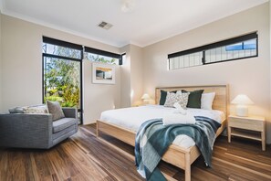 A modern bedroom with a large bed, a sofa, a nightstand, and a window with a view of greenery. - Golf Course Views & Short Walk to Town (Dunsborough)