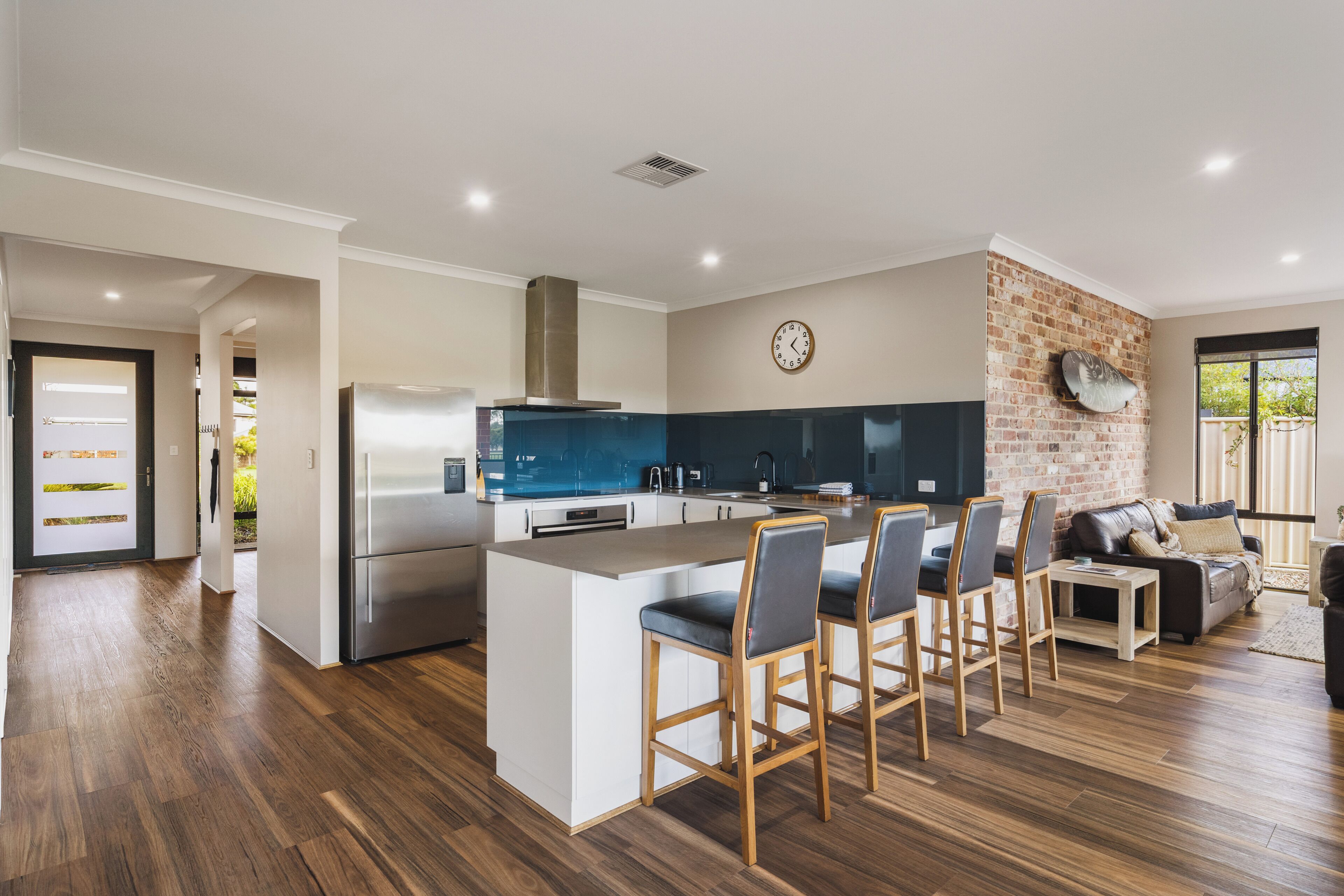 Una cucina moderna con isola centrale, sgabelli da bar, frigorifero e parete decorata con mattoni.