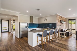 A modern kitchen with a central island, bar stools, a refrigerator, and a brick accent wall. - Golf Course Views & Short Walk to Town (Dunsborough)