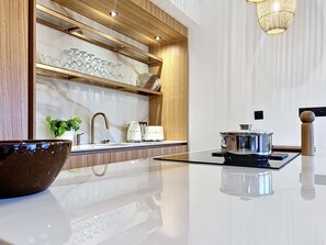 Eine moderne Küche mit Marmor-Spritzschutz, Holzregalen, einem Edelstahlkochtopf auf einem Herd und einer spiegelnden Arbeitsplatte.