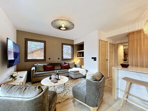 Ein modernes Wohnzimmer mit einer Couch, Sesseln, einem Couchtisch, einem Fernseher und einem Kamin.