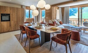 Eine moderne Küche mit Holzvertäfelung, einem Essbereich mit runden Tischen und Stühlen sowie großen Fenstern mit Blick ins Freie.