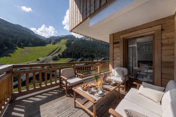 Eine Holzterrasse mit Sitzgelegenheiten, einem Esstisch und Blick auf eine gebirgige Landschaft.