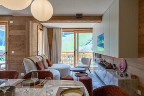 Ein modernes Interieur mit einer Couch, einem Esstisch, Stühlen, einem Kamin und einem großen Fenster mit Bergblick.