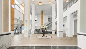 Eine großzügige Lobby mit einer zentralen Blumenkomposition, Marmorboden und einer Treppe im Hintergrund.