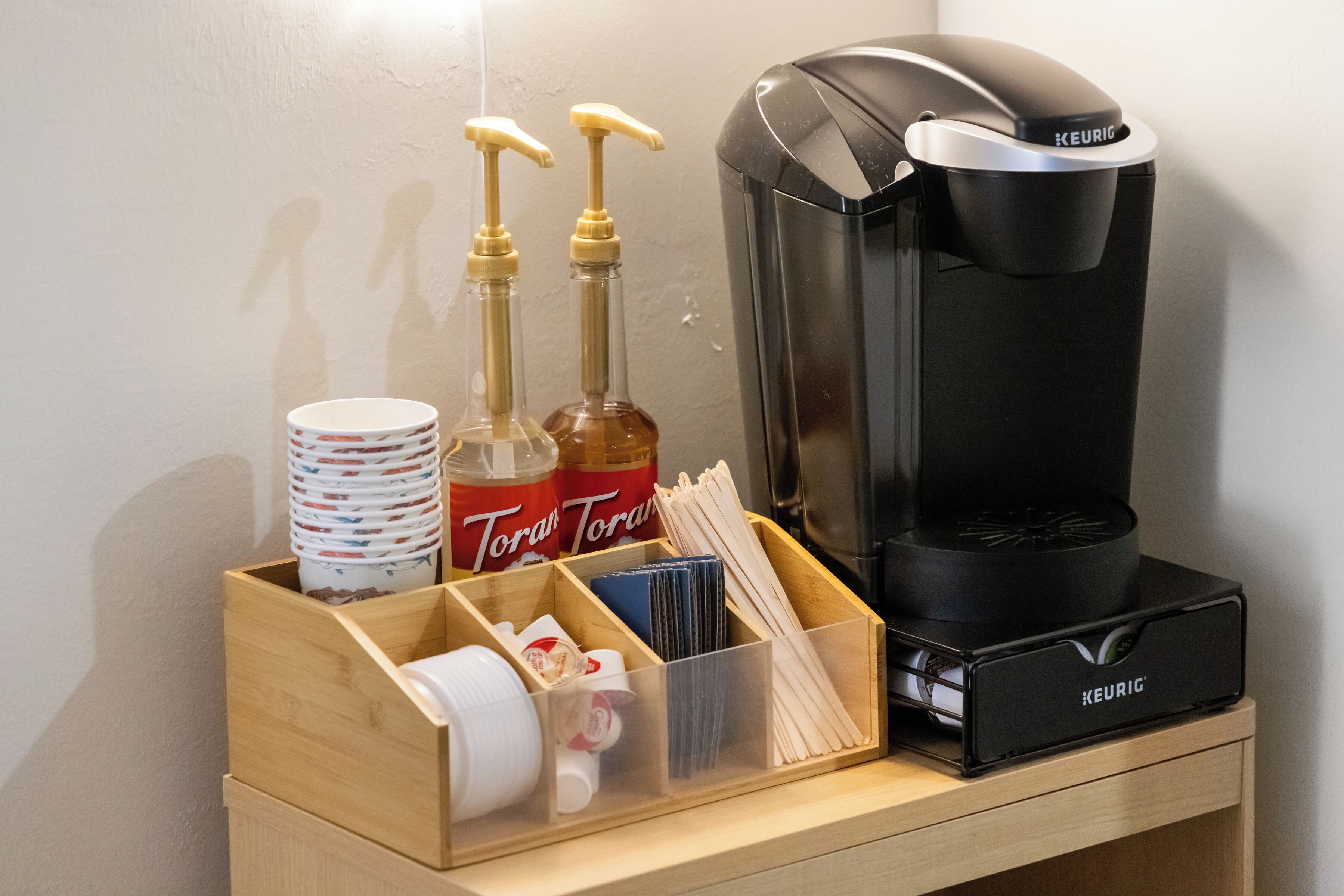 Eine Kaffeemaschine, Flaschen mit Torani-Sirup und ein Spender auf einer Holzablage.
