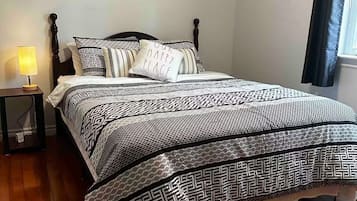 A bedroom with a patterned bedspread, a wall art piece, a bedside lamp, and a window with curtains.