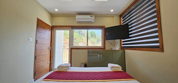 A bedroom with a bed, a window with blinds, a television mounted on the wall, and an air conditioning unit. - ROYAL PALACE STAY (Iritty)