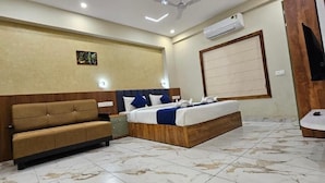 A hotel room with a bed, a sofa, a wooden headboard, a wall-mounted air conditioner, and a television.