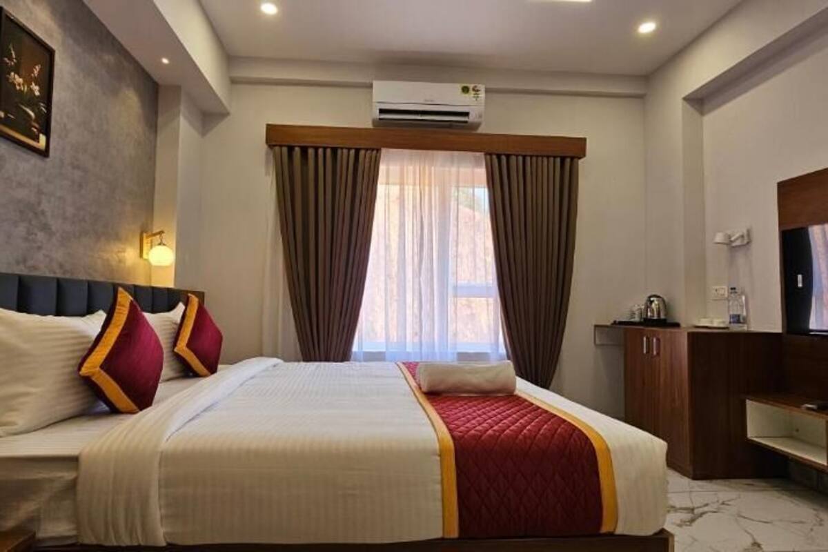 A hotel room with a bed, a TV, a desk, and a window with curtains.