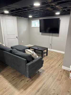 Ein modernes Wohnzimmer mit grauem Sofa, einem Couchtisch und einem flachbildfernseher an der Wand.
