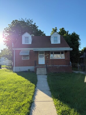 A two-story brick house with a front porch, a small front yard, and a clear sky. - Modern Suite near Downtown Baltimore (Baltimore)